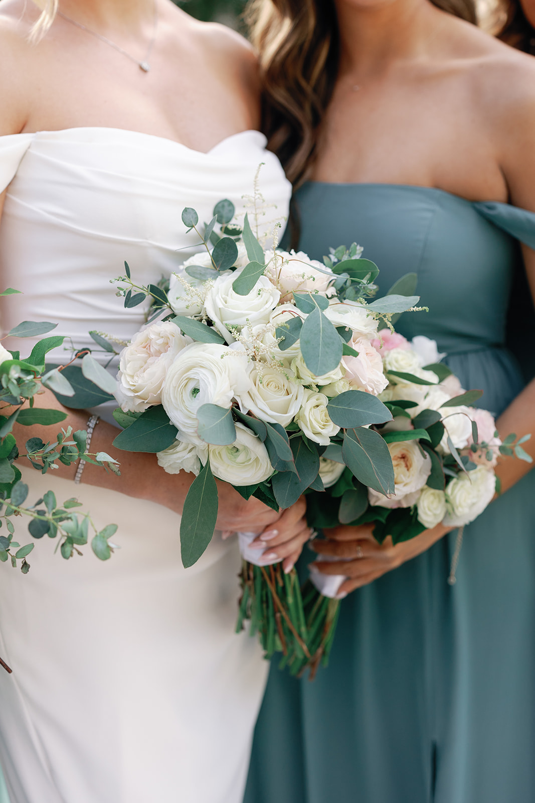 Details of a bride standing with a bridesmaid holding their matching white rose bouquets