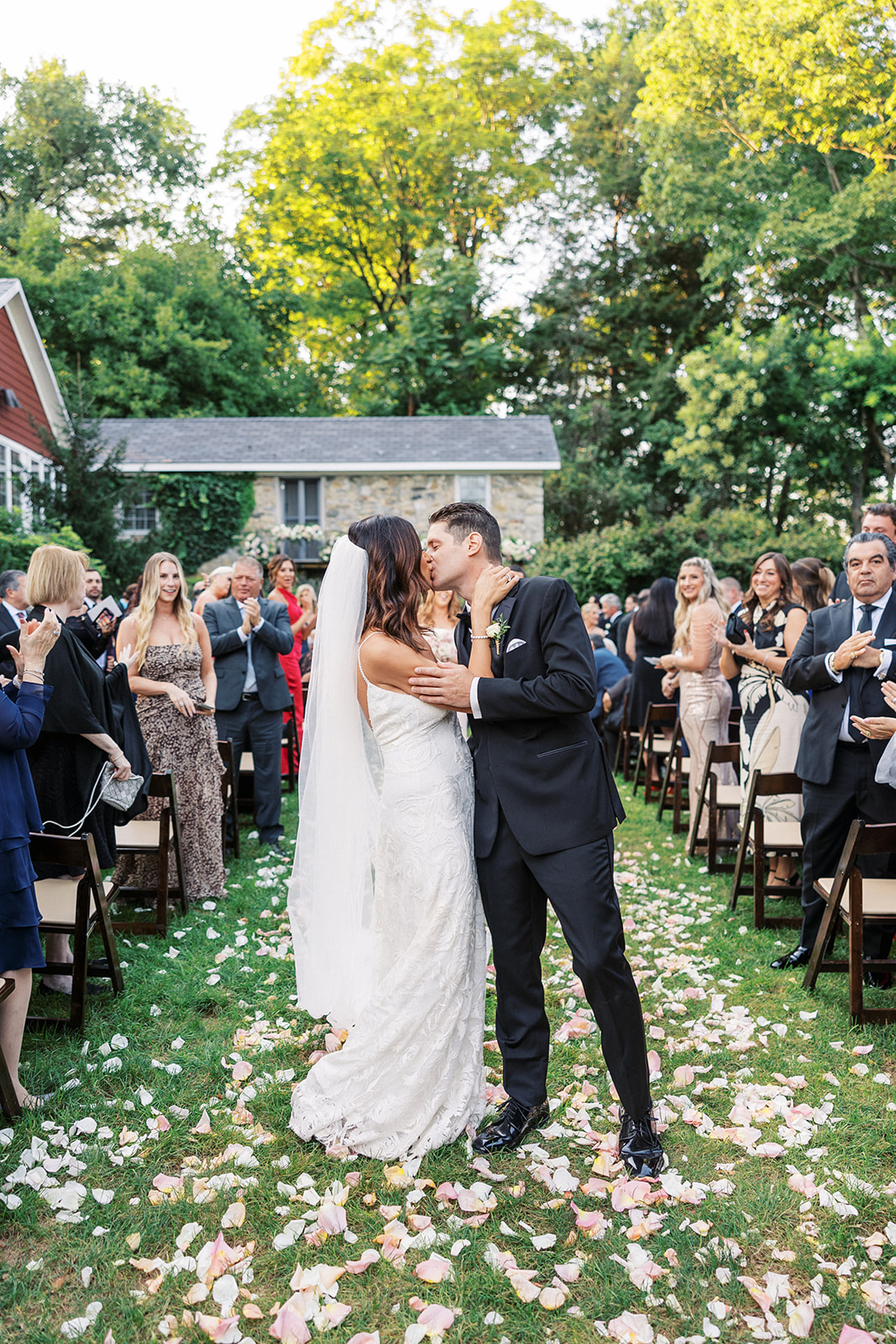 Newlyweds kiss in the flower petal covered aisle while guests clap and cheer