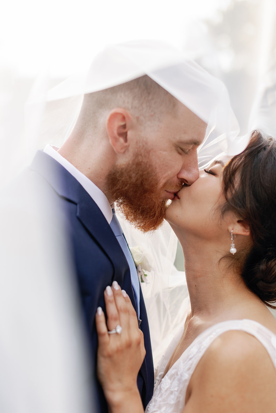 Newlyweds kiss under the veil in a blue suit and lace dress