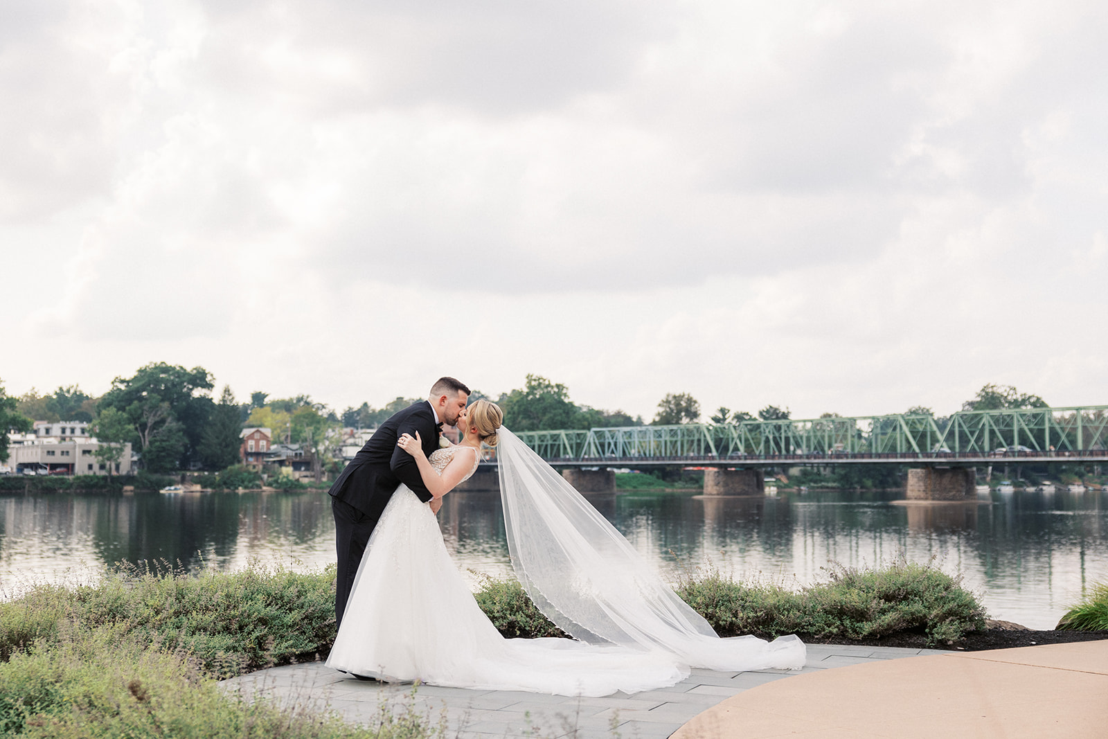 Newlyweds kiss on a lakefront sidewalk on a cloudy day