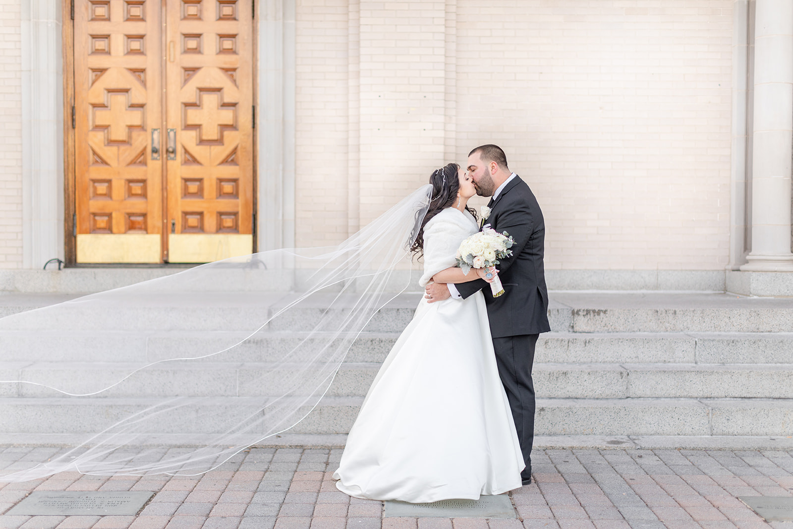 Newlyweds kiss on a windy day outside their church ceremony