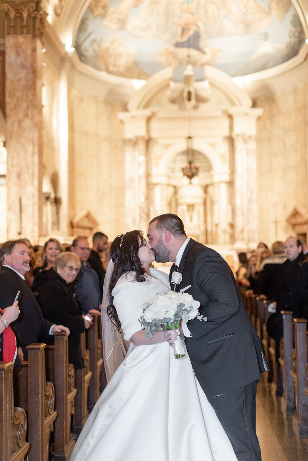 Newlyweds kiss in the church aisle with guests smiling at them to end their ceremony