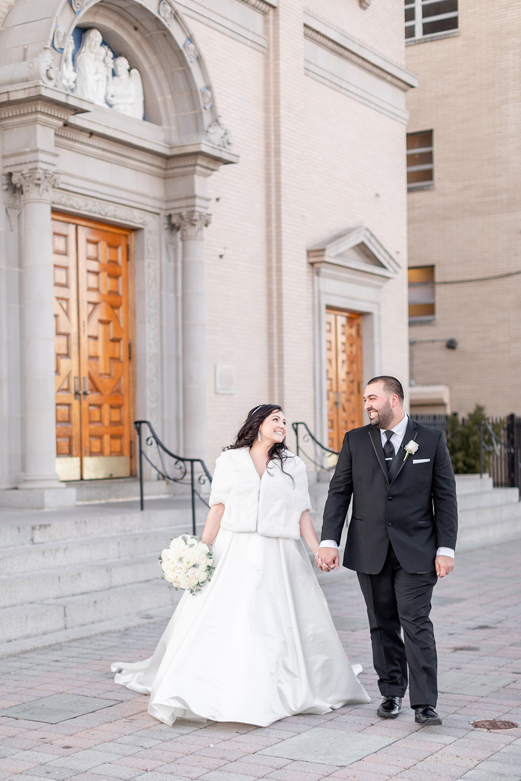 Newlyweds walk on a sidewalk at the church before their Nanina’s In the Park wedding reception