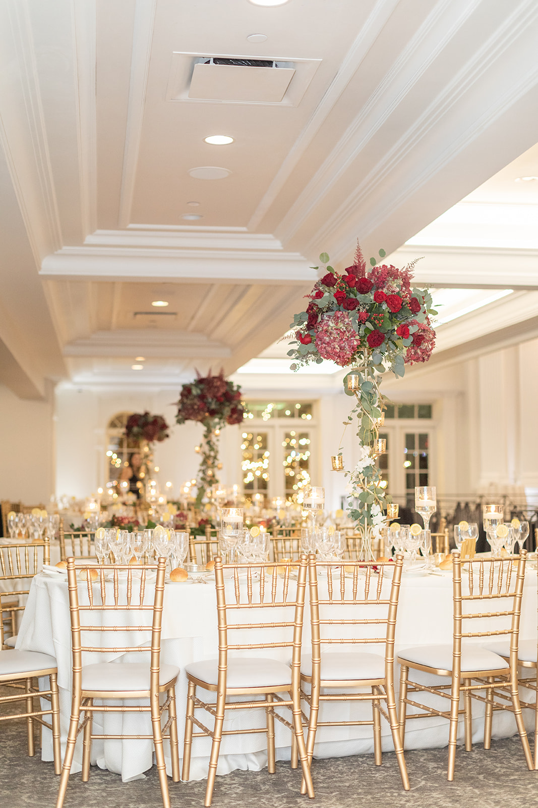 A look at the tall red rose centerpieces on the wedding reception tables with gold chairs