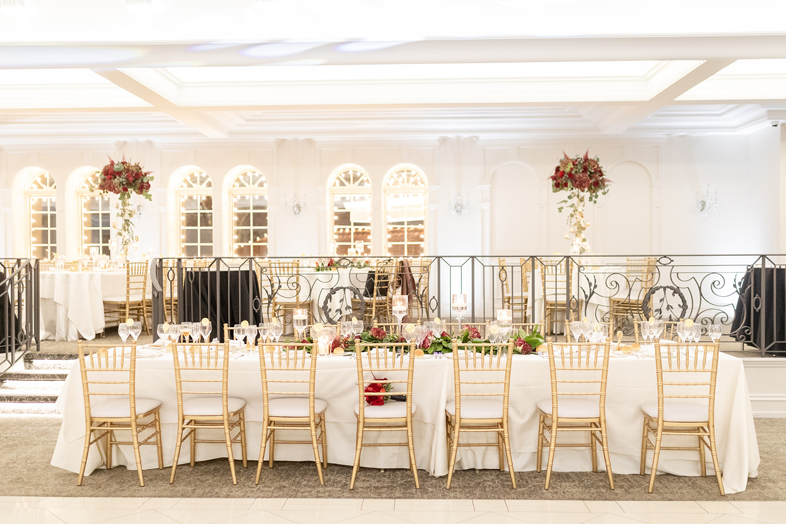 A view of a long Nanina's In the Park wedding reception table with gold chairs and white linens