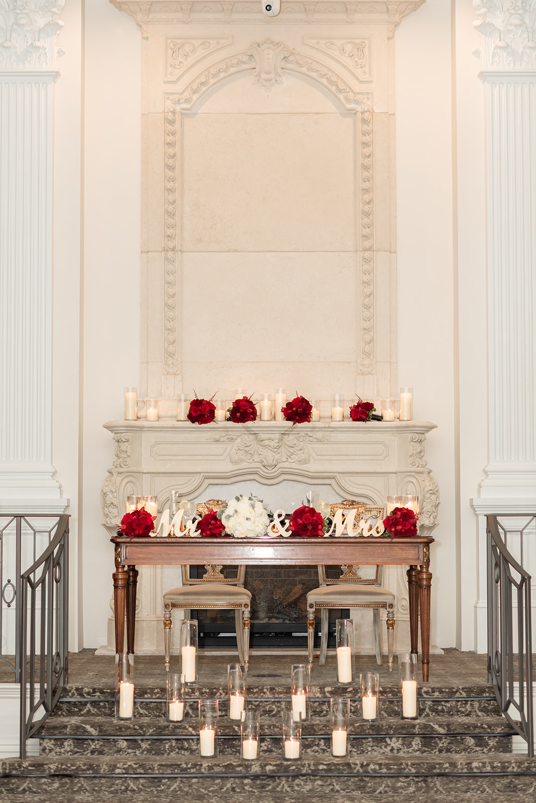 A view of the Nanina’s In the Park head table and ornate fireplace for the newlyweds with red and white roses and candles