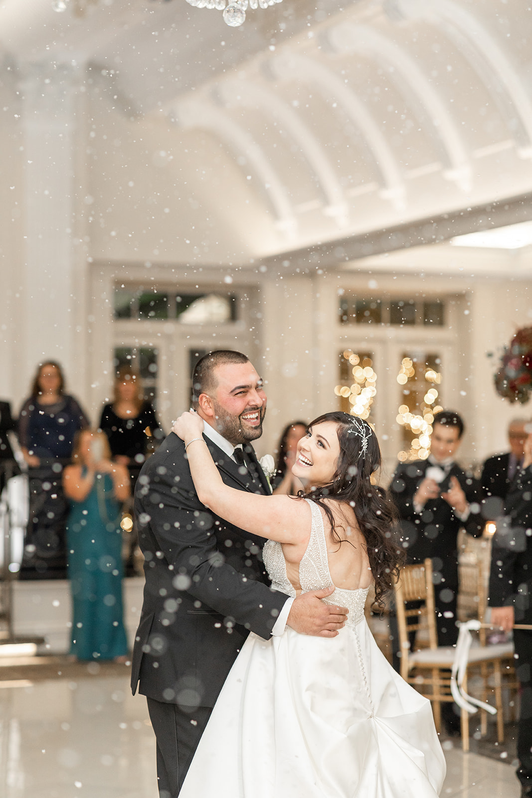 Newlyweds dance under a snow machine while laughing on the Nanina’s In the Park dance floor