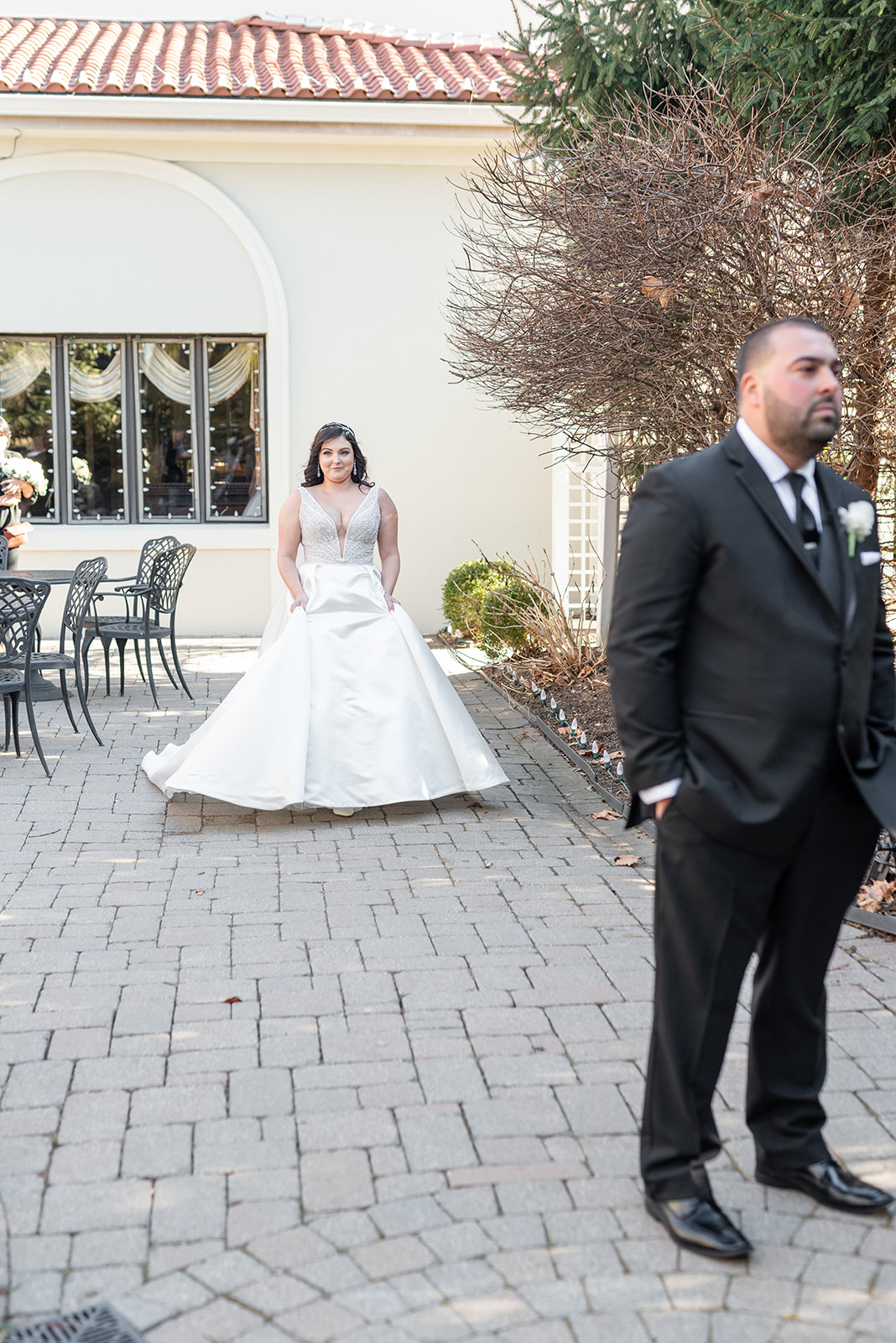 A groom waits while his bride approaches from behind for their first look in a garden