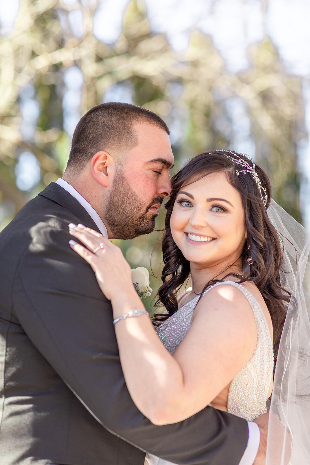 A bride smiles while her husband leans in to kiss her cheek in the gardens at their wedding