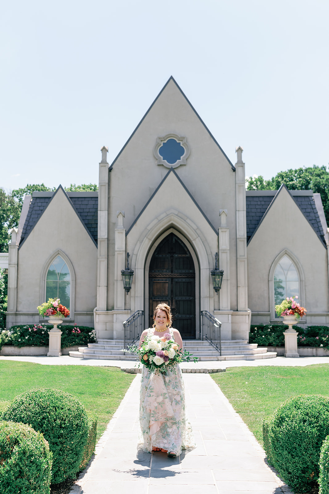 A bride walks down the aisle in front of the chapel holding her bouquet