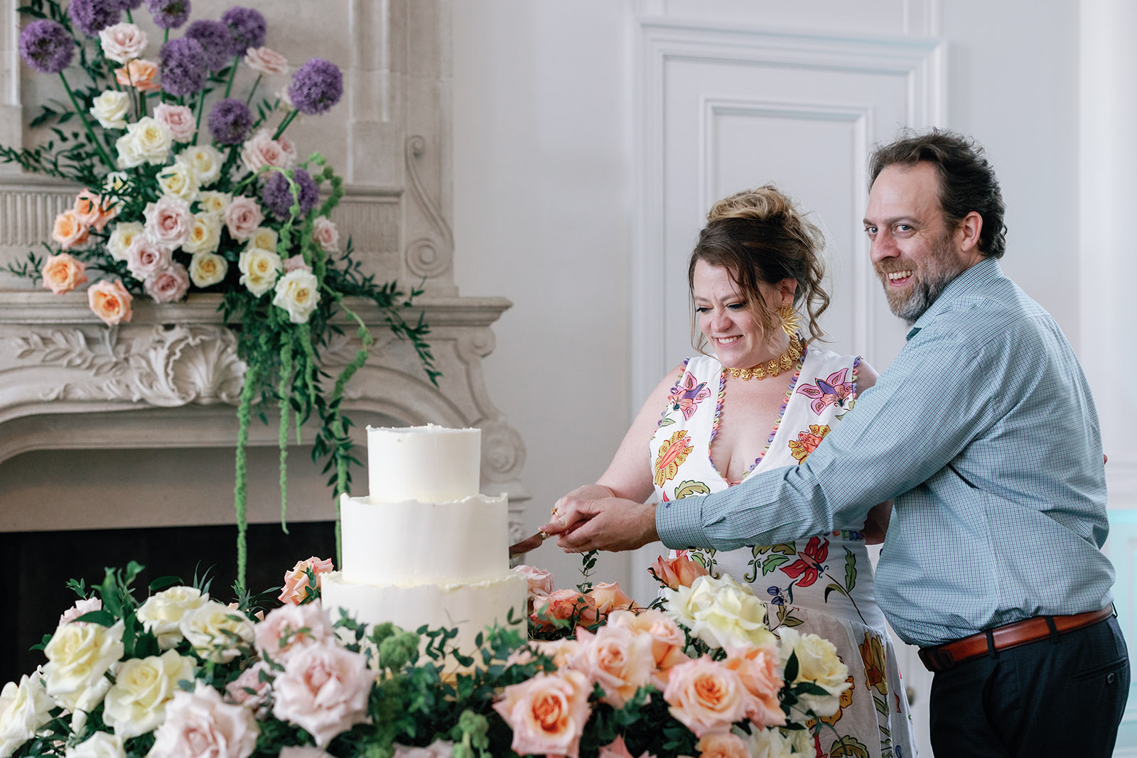 Newlyweds in a colorful dress and blue shirt cut their three tier cake surrounded by roses of many colors
