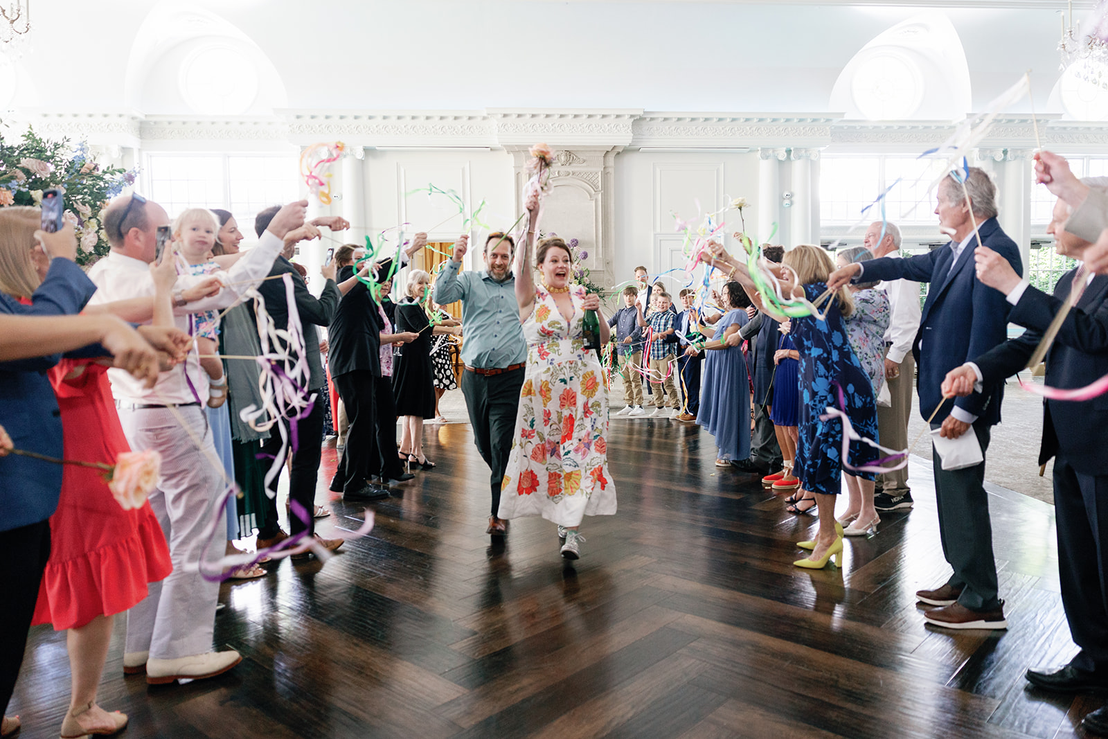 Newlyweds Celebrate while walking up an aisle under colorful streamers waved by guests at their Park Chateau Wedding