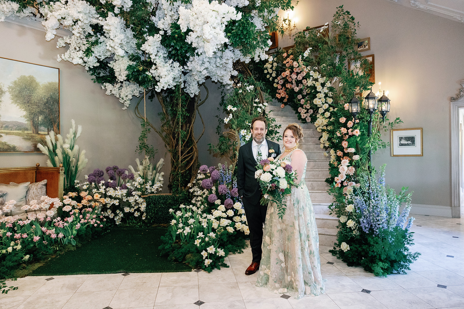 Newlyweds stand at the base of the Park Chateau Wedding venue grand staircase covered in colorful flowers