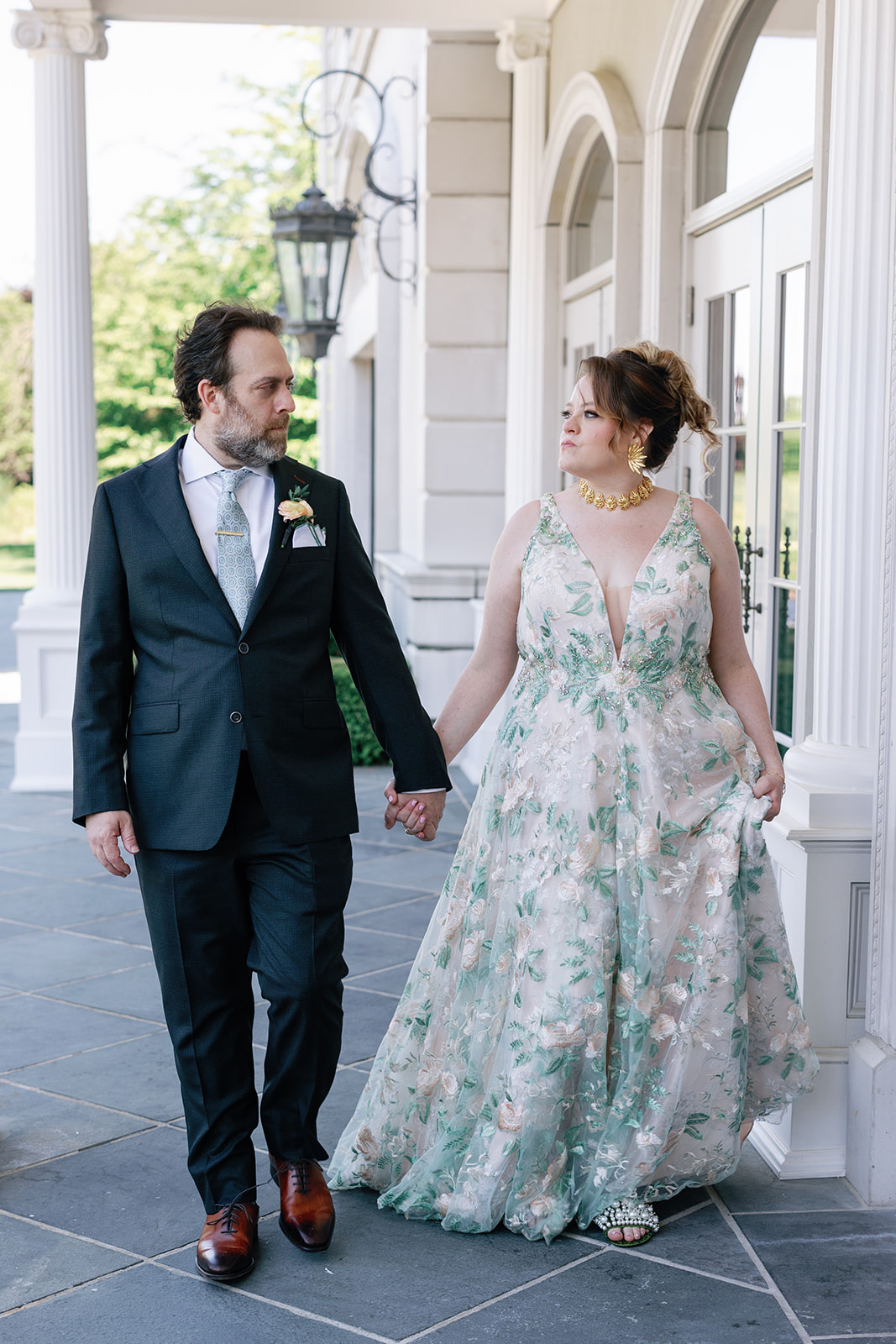 Newlyweds walk on the front porch holding hands in a suit and green dress