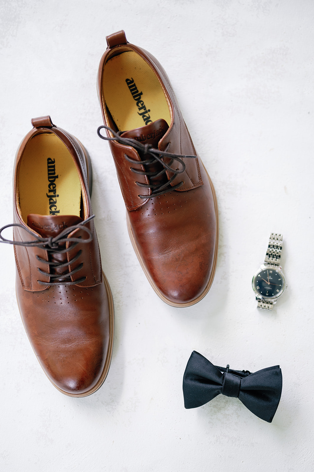 A groom's shoes, bowtie and watch sitting on a white table